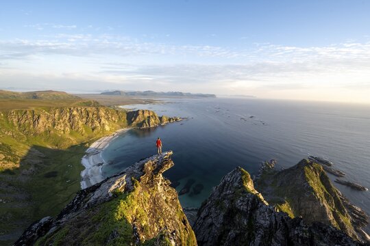 Evening mood, mountaineer standing on a rocky outcrop on the summit of M&aring;tind, view of coastal landscape, H&oslash;yvika beach and sea, M&aring;tinden, And&oslash;ya island, Vester&aring;len, Nordland Norway