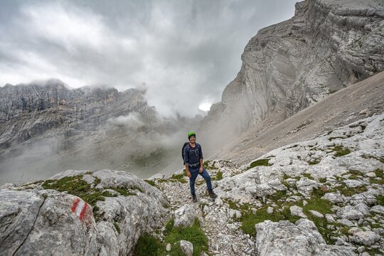 Hiker, climber on a trail between rocky cloudy mountains at Forcella Sore de la Cengia, Sorapiss circumnavigation, Dolomites, Belluno, Italy