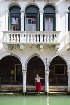 Young woman standing in a portico by a canal, Venice, Veneto, Italy