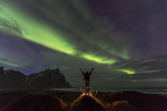 Night shot, man watching Northern Lights (Aurora borealis), Black sand beach, mountains Klifatindur, Eystrahorn and Kambhorn, headland Stokksnes, massif Klifatindur, Austurland, East Iceland, Iceland