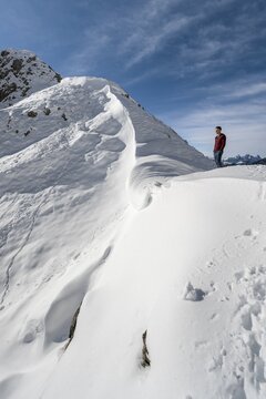 Hiker standing at a snow cornice at a saddle, hiker in the snow at Roggentalsattel, hiking trail to Ammergauer Hochplatte, in autumn, Ammergau Alps, Bavaria, Germany