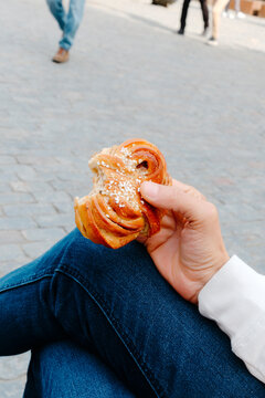 a man holds a bitten kanelbulle in a public square