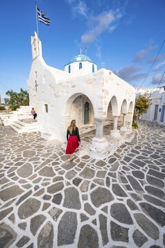 Tourist with red dress, Blue and White Greek Orthodox Church Agios Nikolaos with Greek Flag, Parikia, Paros, Cyclades, Aegean Sea, Greece