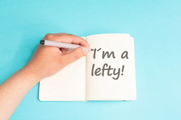 I am a lefty standing on notebook, writing with left hand, pen and table, left handed concept, handwriting a message