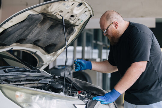 Garage Mechanic worker in auto service center working check and change engine oil under hood.