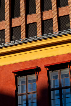 Red lower walls and yellow trim sit below a brick facade, with windows and shadow giving urban architecture a warm building exterior