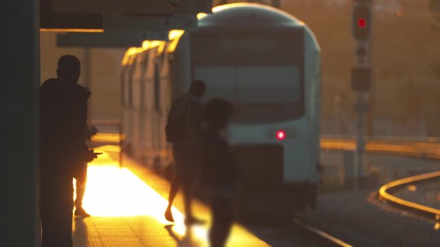 Train arrives at station during sunset with people waiting and shadows on platform in a busy urban setting
