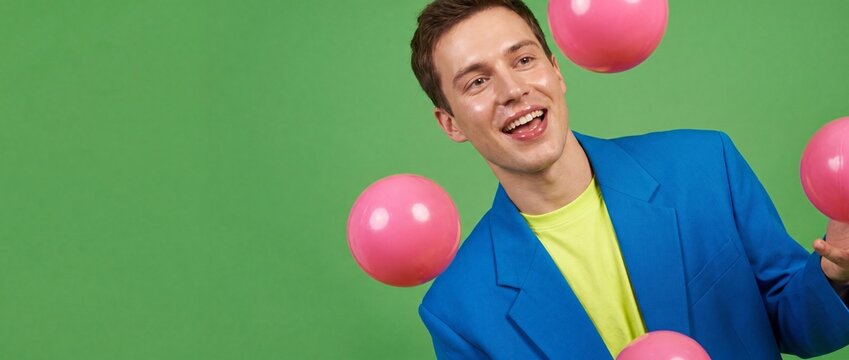 Happy man juggling pink balls in vibrant blue suit blazer jacket over lime green background, smiling cheerful guy posing playful creative business concept, modern office party celebrating success joy.