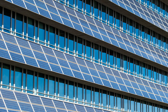 Blue solar panels cover a glass facade in sustainable architecture, while windows and urban building grid lines reflect daylight across the exterior