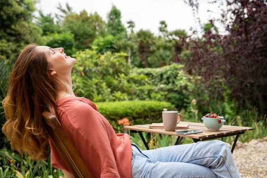 Smiling woman with eyes closed relaxing while sitting on chair in garden