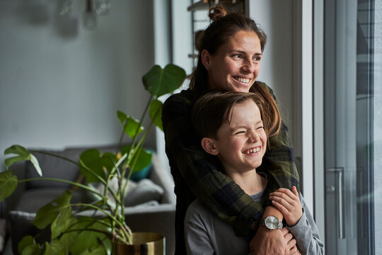 Happy mother and son looking through window while standing at home