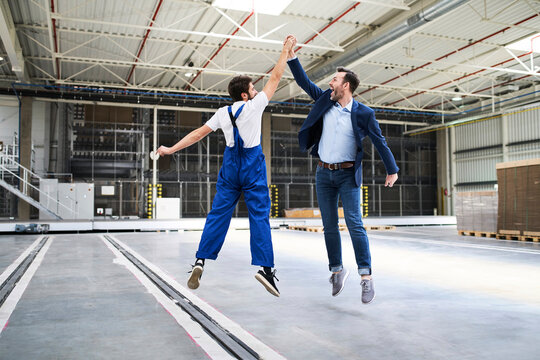 Excited businessman and worker jumping and high fiving in a factory