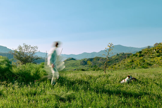 Blurred figure walking dog in green mountain meadow