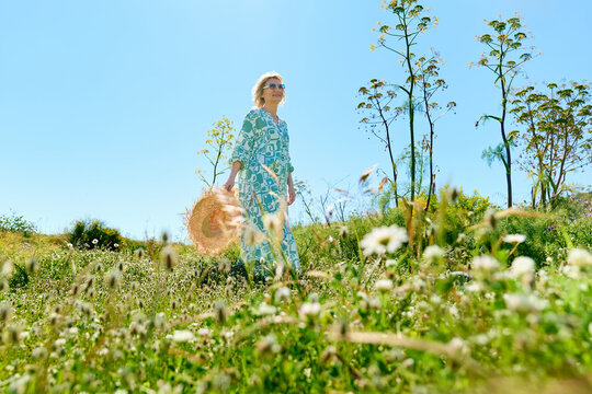 Woman walking in a sunny wildflower meadow with a straw hat