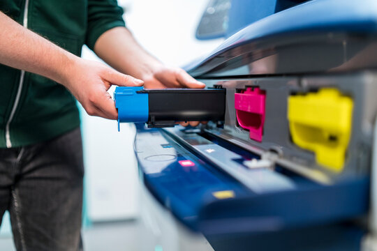 Close-up of teenager working at color printer inserting print cartridge