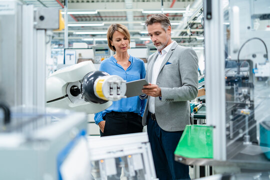 Businessman with tablet and woman talking at assembly robot in a factory
