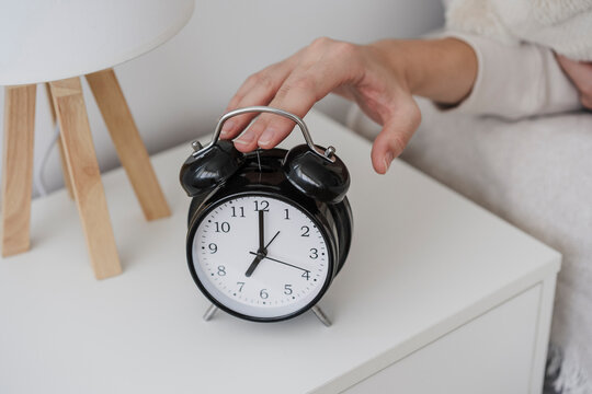 Hand of woman turning off alarm clock on night table