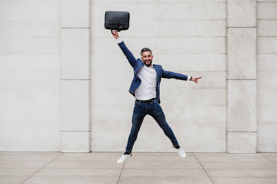 Happy businessman with briefcase jumping on footpath