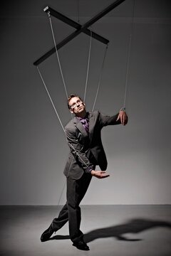 Businessperson controlled by strings like a puppet in a studio