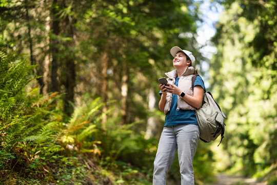 Smiling hiker holding smartphone on a forest footpath