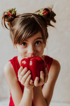 Playful girl holding red pepper with strawberry in hair