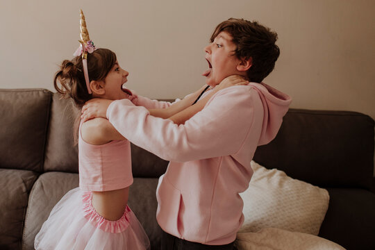 Siblings in pink clothing playfully fighting on a sofa at home