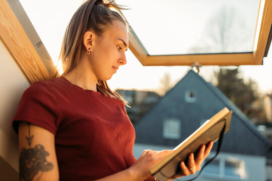 Young woman reading book at the window in backlight