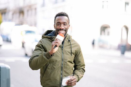 Smiling male journalist with microphone standing on street in city