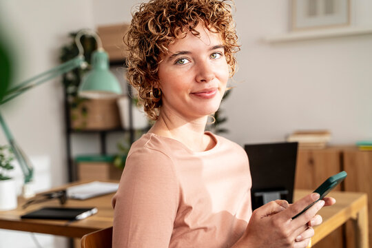 Smiling woman in cozy organized home office using smartphone