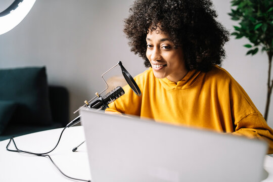 Young woman podcasting while looking at laptop at home