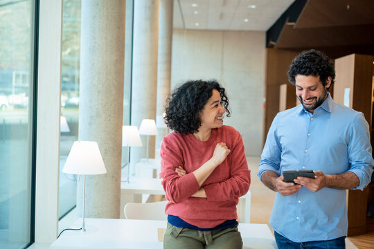 Happy man and woman discussing over tablet PC in library