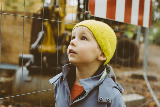 Portrait of little boy with yellow woolly hat in front of construction site