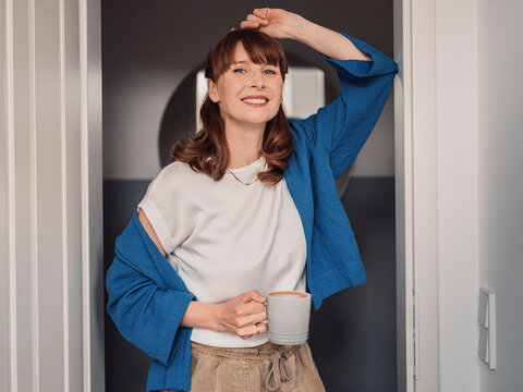 Smiling female homeowner standing in doorframe holding coffee
