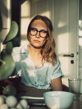 Happy woman with eyeglasses sitting at a home table at sunset