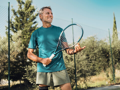 Smiling tennis player with knee brace holding racket outdoors