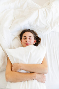 Smiling young woman embracing pillow while sleeping on bed