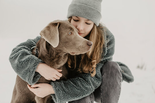 Portrait of teenage girl crouching in snow and embracing Labrador Retriever