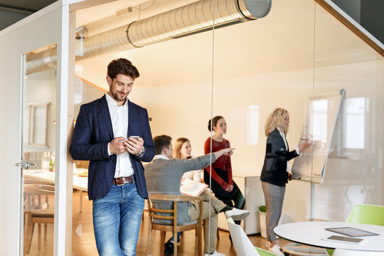 Businessman using cell phone in office with a meeting in background