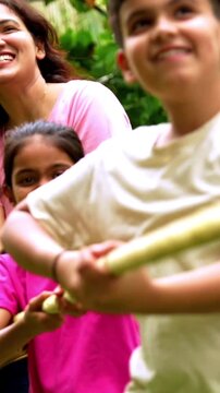 Indian family playing tug of war rassi khech in home garden, spending quality fun time together enjoying outdoor sports, cheerful Asian parents children bonding through traditional backyard activity