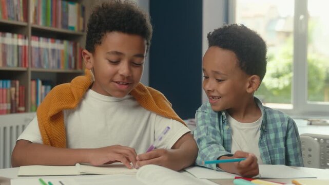 Two little boys African American children writing exercise study in library funny smiling sons kids communicating friendly cooperating write studying learning teamwork learn friendship back to school