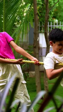 Indian family playing tug of war rassi khech in home garden, spending quality fun time together enjoying outdoor sports, cheerful Asian parents children bonding through traditional backyard activity