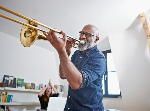Portrait of man playing trombone at home office