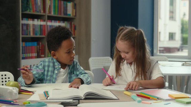 Two multiethnic little kids wring in textbook studying communicating friendly multiracial children African American boy Caucasian girl innocence pupils schoolchildren study write schoolwork in school