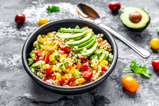 Bowl of bulgur salad with bell pepper, tomatoes, avocado, spring onion and parsley