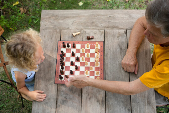 Grandfather and granddaughter playing chess on table