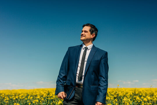 Smiling businessman with tablet standing in yellow rapeseed field