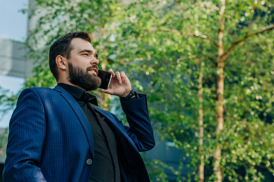 Businessperson in suit talking on smartphone outdoors by trees