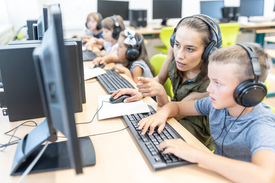 Teacher gesturing by student wearing headphones doing E-learning at school