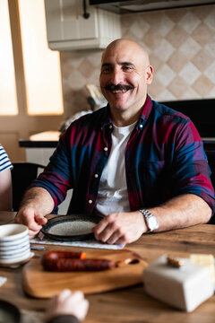Man with a moustache smiling at home in the kitchen during breakfast