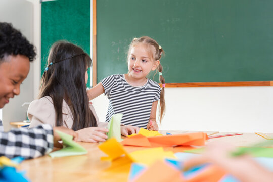 Diverse students learning to make paper crafts in elementary classroom, Happy children collaborating on creative school project, Primary school students working together on handmade art activity